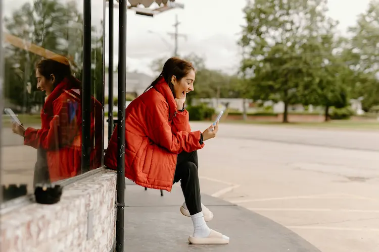 Chica con chaqueta roja sonriendo mientras mira su celular